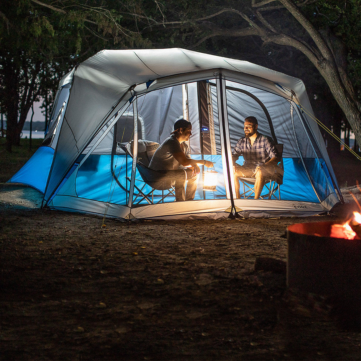 10 Person Lighted Instant Cabin Tent Lifestyle with two friends sitting in chairs in screen room at night