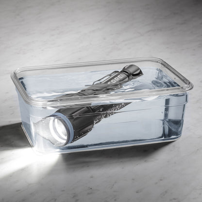 Dark gray CORE 2000 lumen rechargeable flashlights with blue accents, turned on in a clear container of water. 